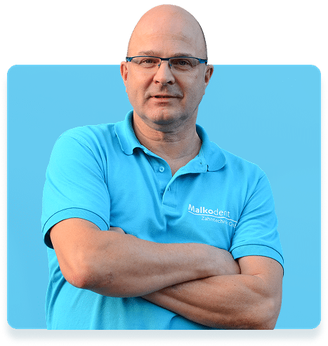 Porträt eines Mannes in hellblauem Malkodent-Poloshirt mit verschränkten Armen vor blauem Hintergrund – Geschäftsführer von Malkodent Zahntechnik